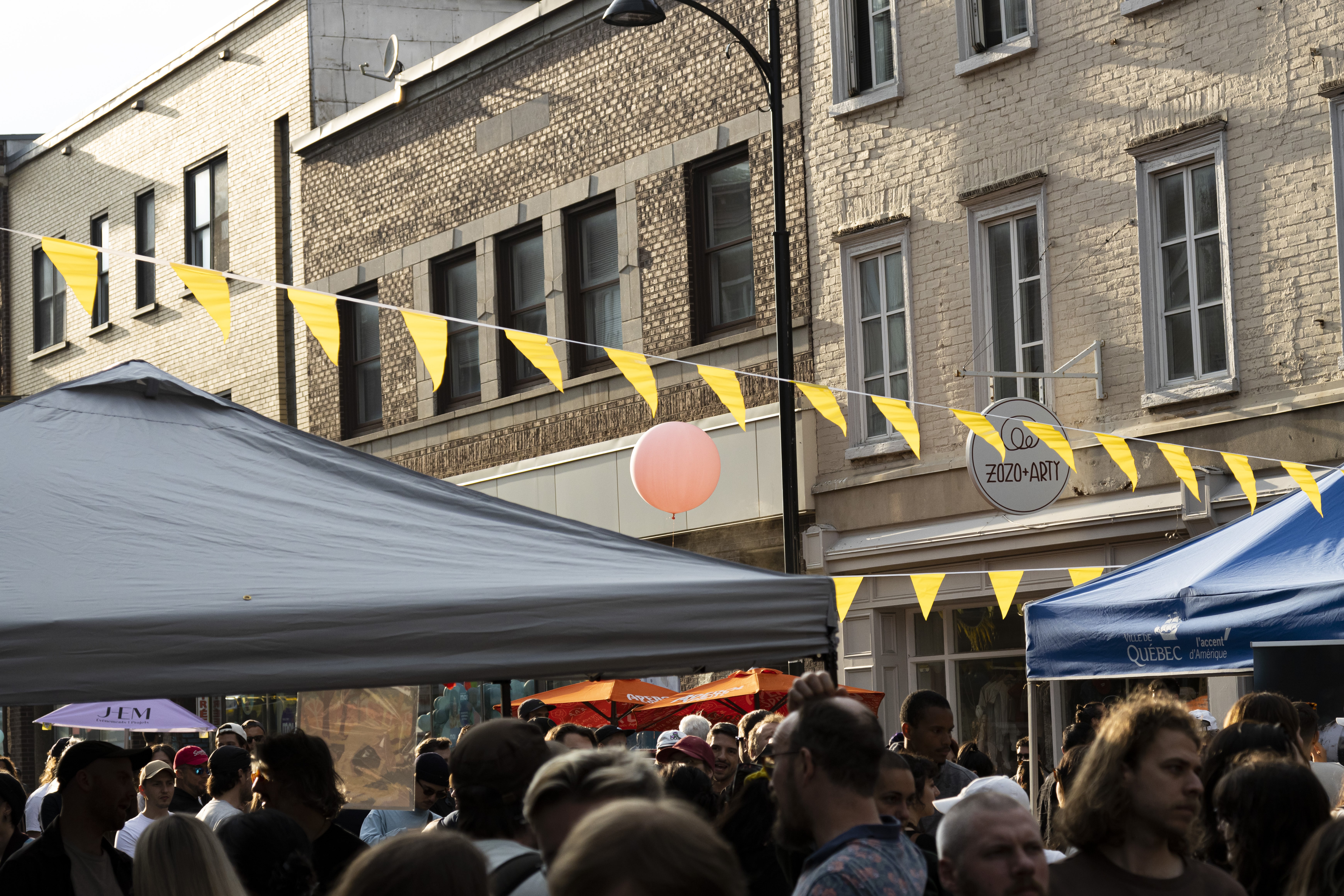 Vue d'une rue animée lors d'un événement dans le quartier Saint-Sauveur avec des gens rassemblés sous une tente et une décoration de ballons et guirlandes.