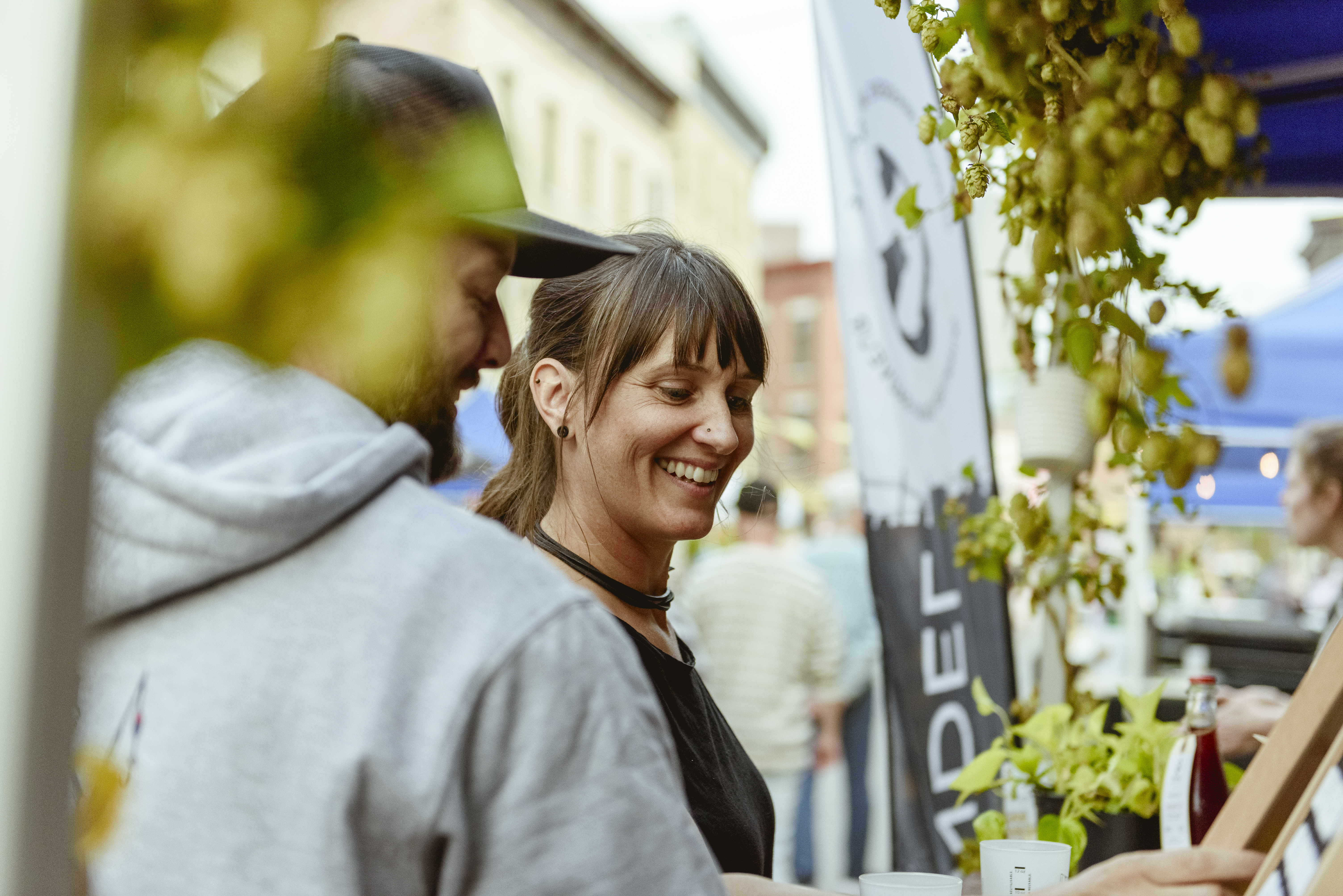 Portrait d'une femme souriante avec une coupe de cheveux au carré, portant un collier ras du cou, sur fond de rue animée.